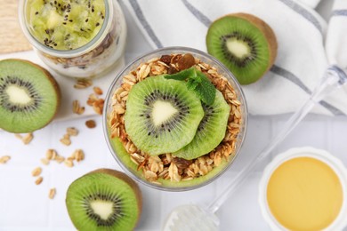 Delicious dessert with kiwi, muesli and fresh cut fruits on white table, flat lay