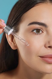 Photo of Beautiful young woman applying serum onto her face on light blue background, closeup