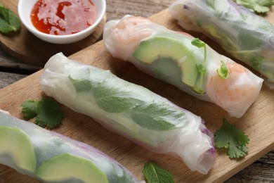 Photo of Delicious spring rolls and sauce on wooden table, closeup