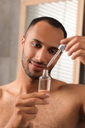 Photo of Handsome man with cosmetic serum in hands indoors