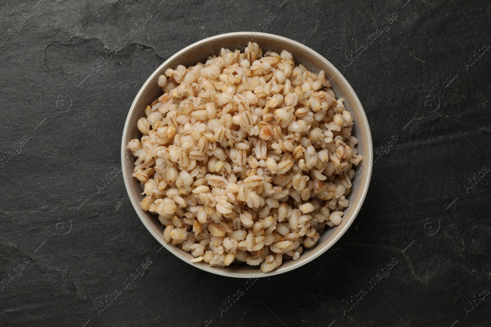 Photo of Tasty pearl barley porridge in bowl on dark textured table, top view