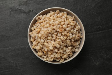 Photo of Tasty pearl barley porridge in bowl on dark textured table, top view