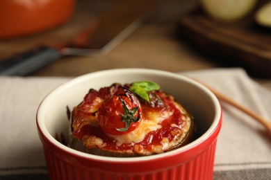 Photo of Baked eggplant with tomatoes, cheese and basil in ramekin on table, closeup