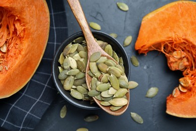 Photo of Bowl with seeds, wooden spoon and cut pumpkin on black table, flat lay