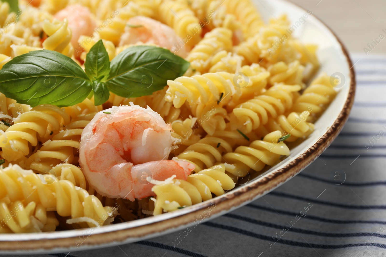 Photo of Plate of delicious pasta with shrimps, basil and parmesan cheese on tablecloth, closeup