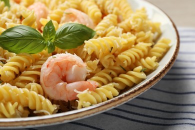 Plate of delicious pasta with shrimps, basil and parmesan cheese on tablecloth, closeup