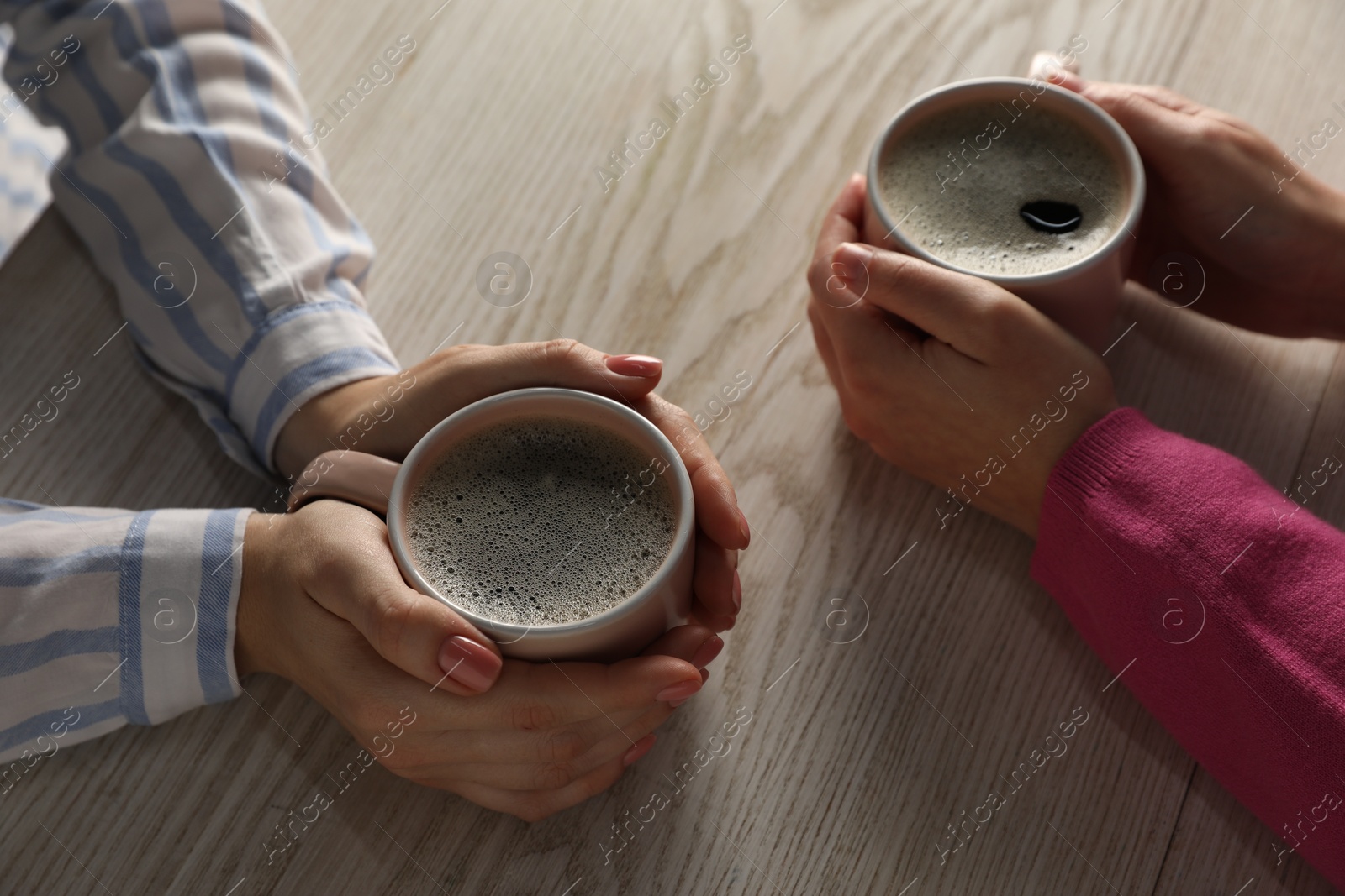 Photo of Women with cups of hot coffee at light wooden table, closeup