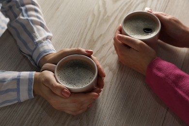 Photo of Women with cups of hot coffee at light wooden table, closeup