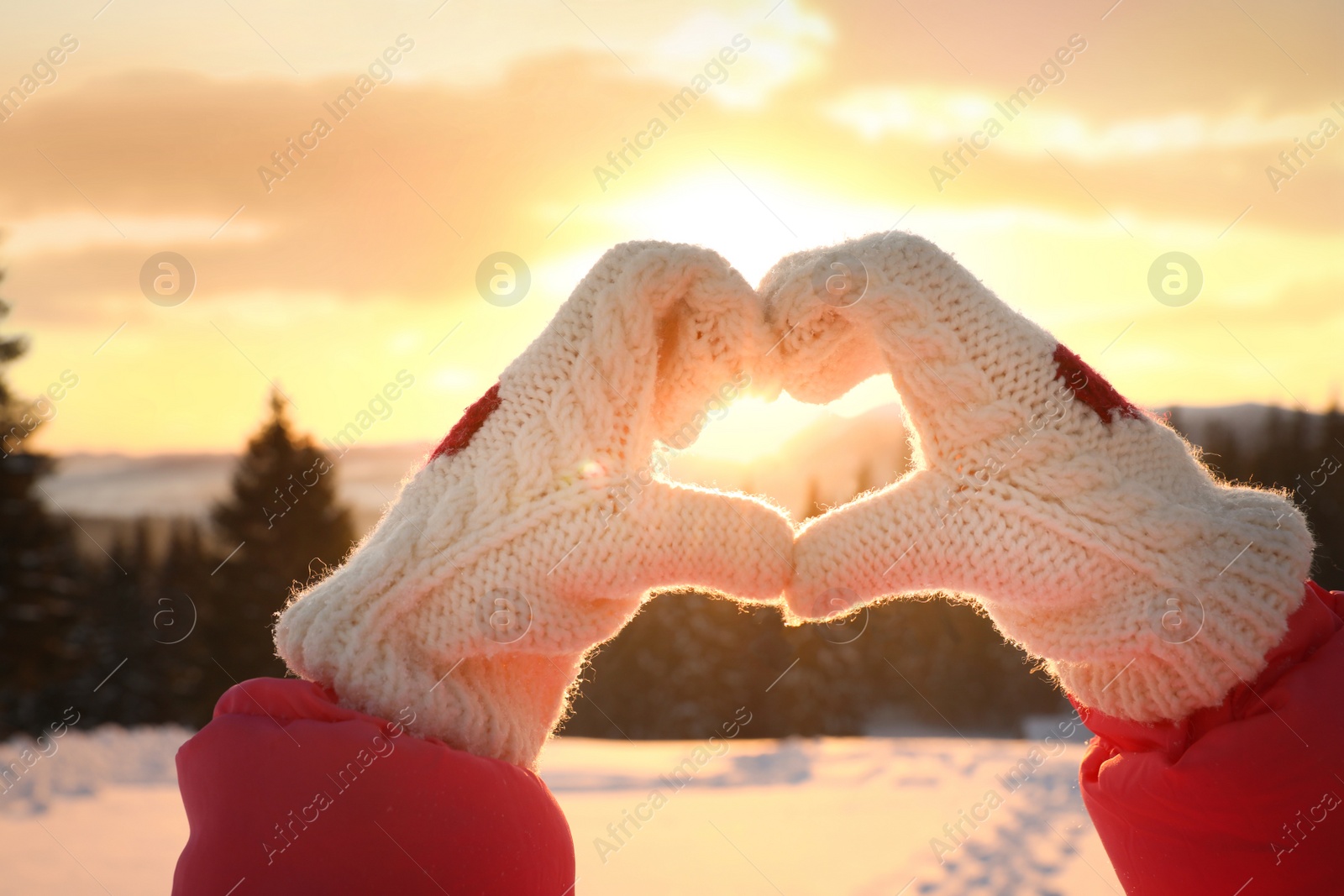 Photo of Woman making heart with hands outdoors at sunset, closeup. Winter vacation