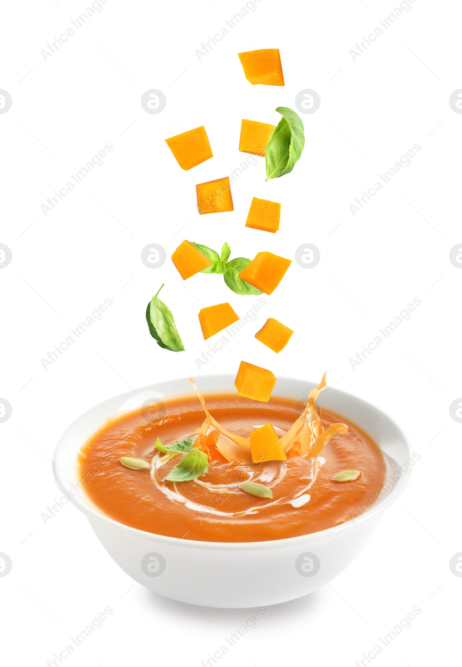 Image of Ingredients falling into bowl of homemade pumpkin soup on white background 