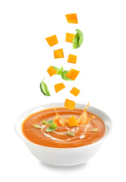 Image of Ingredients falling into bowl of homemade pumpkin soup on white background 