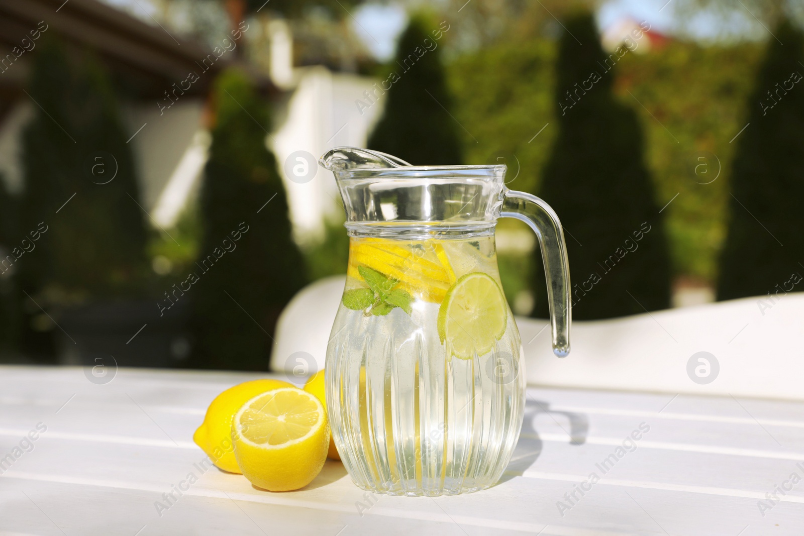 Photo of Jug of water with lemons and mint on white wooden table outdoors