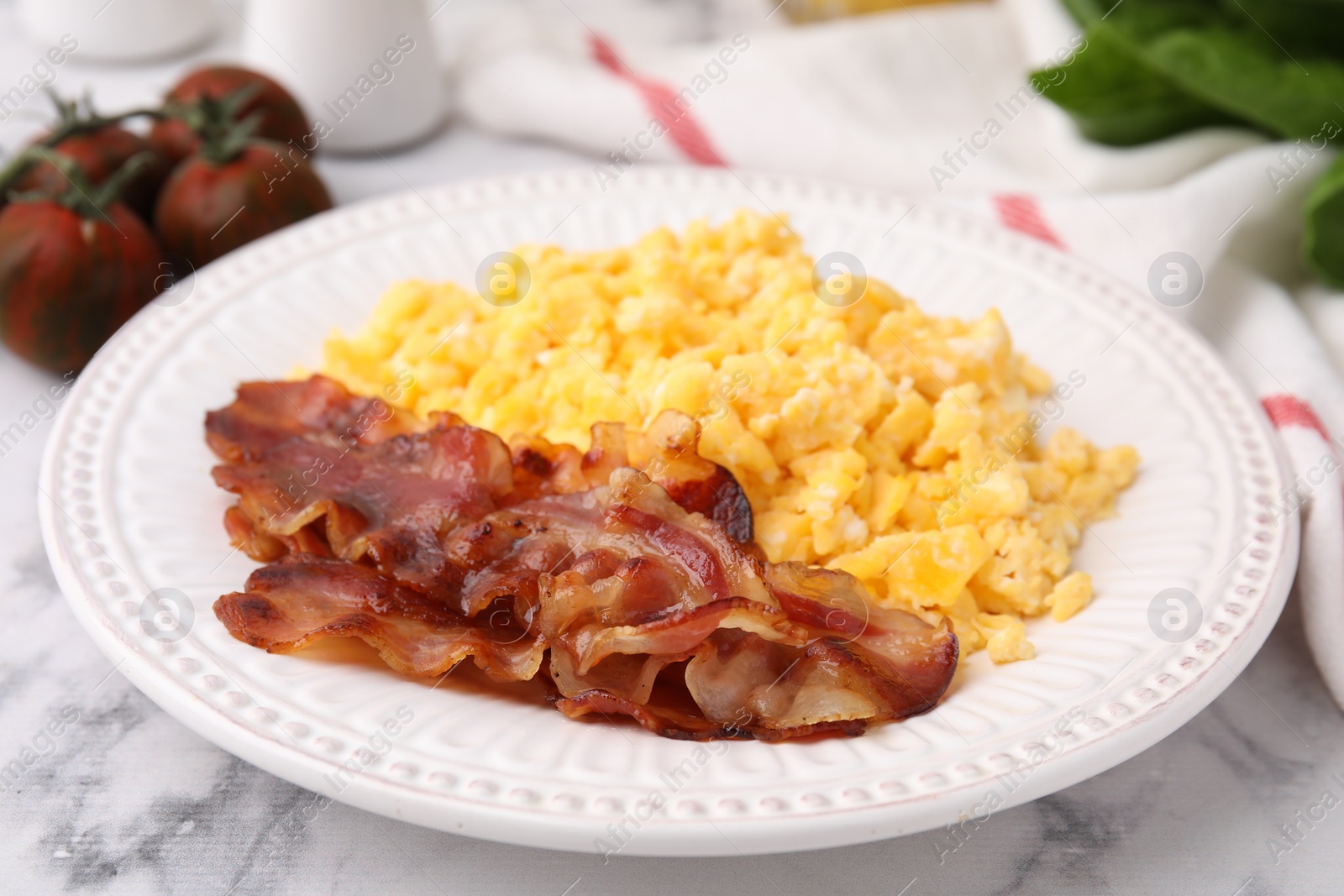 Photo of Delicious scrambled eggs with bacon in plate on white marble table, closeup