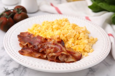 Photo of Delicious scrambled eggs with bacon in plate on white marble table, closeup