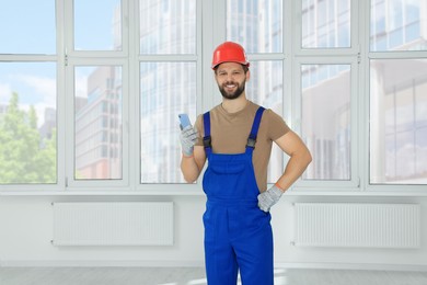 Photo of Professional repairman in uniform with phone indoors, space for text