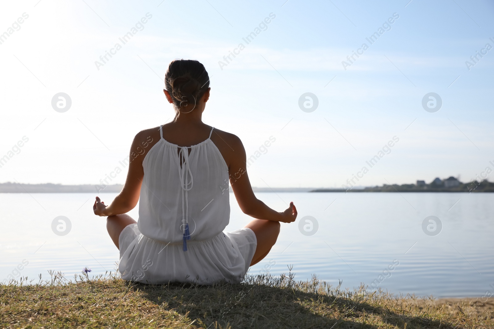 Photo of Young woman meditating near river at sunset. Nature healing power