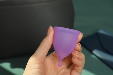 Woman holding violet menstrual cup on blurred background, closeup