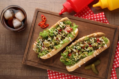 Photo of Tasty hot dogs with chili, lettuce, pickles and sauces served on wooden table, flat lay