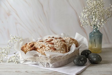 Photo of Delicious Italian Easter dove cake (traditional Colomba di Pasqua), decorated eggs and flowers on white wooden table. Space for text