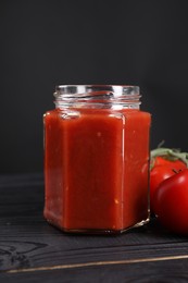 Photo of Delicious ketchup in jar on black wooden table, closeup. Tomato sauce