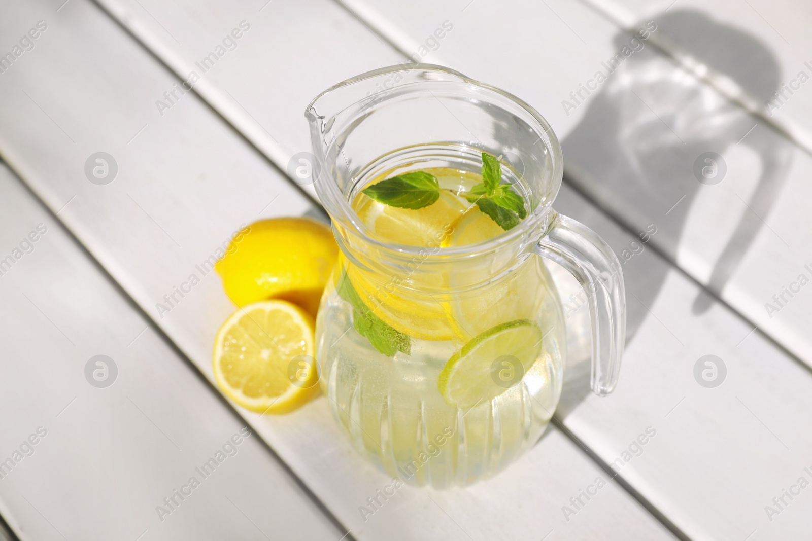 Photo of Jug of water with lemons and mint on white wooden table, above view