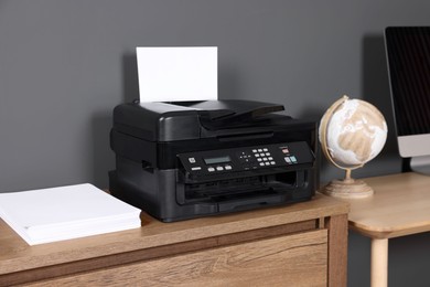 Modern printer with paper near computer on wooden desk at home