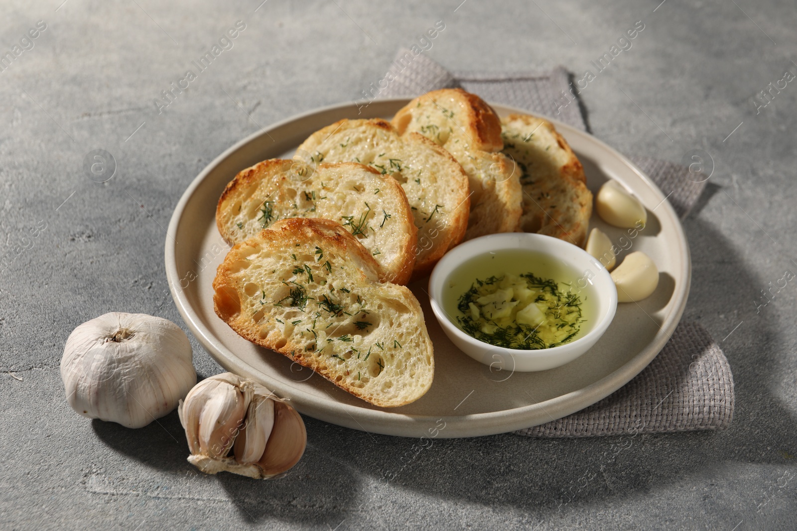 Photo of Tasty baguette with garlic and dill served on grey textured table