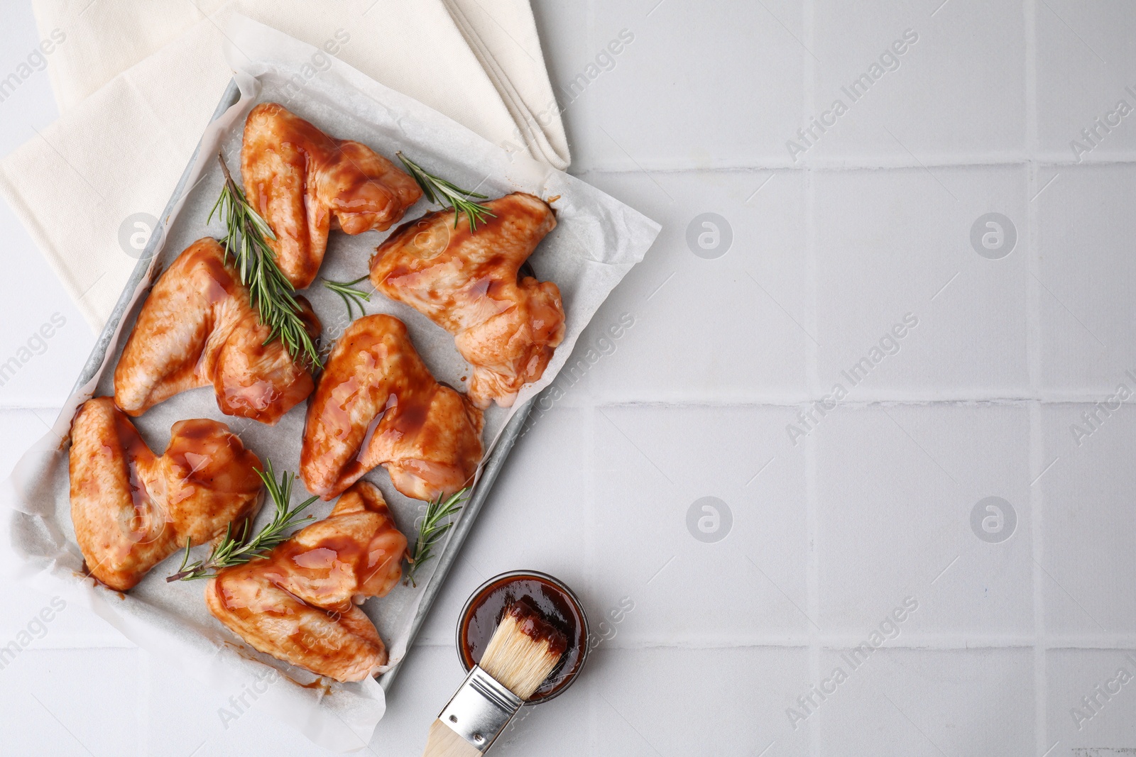 Photo of Raw chicken wings, rosemary, marinade and basting brush on light tiled table, flat lay. Space for text