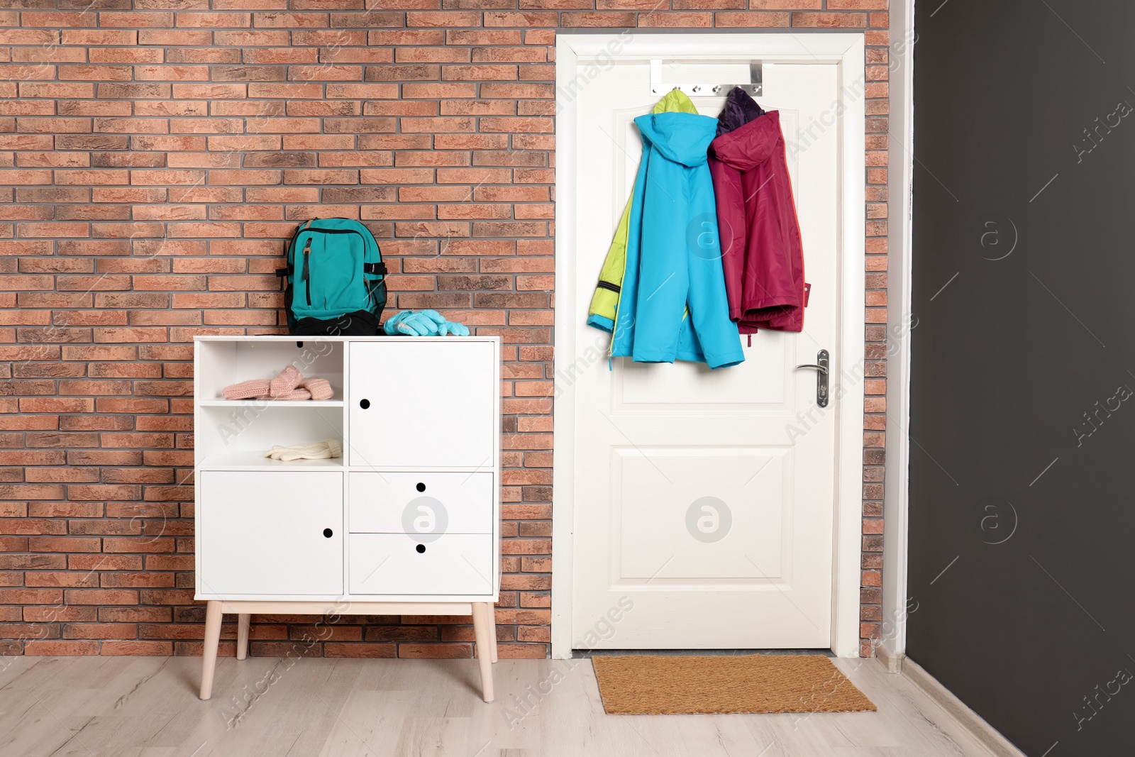 Photo of Stylish hallway interior with chest of drawers and clothes hanging on white door