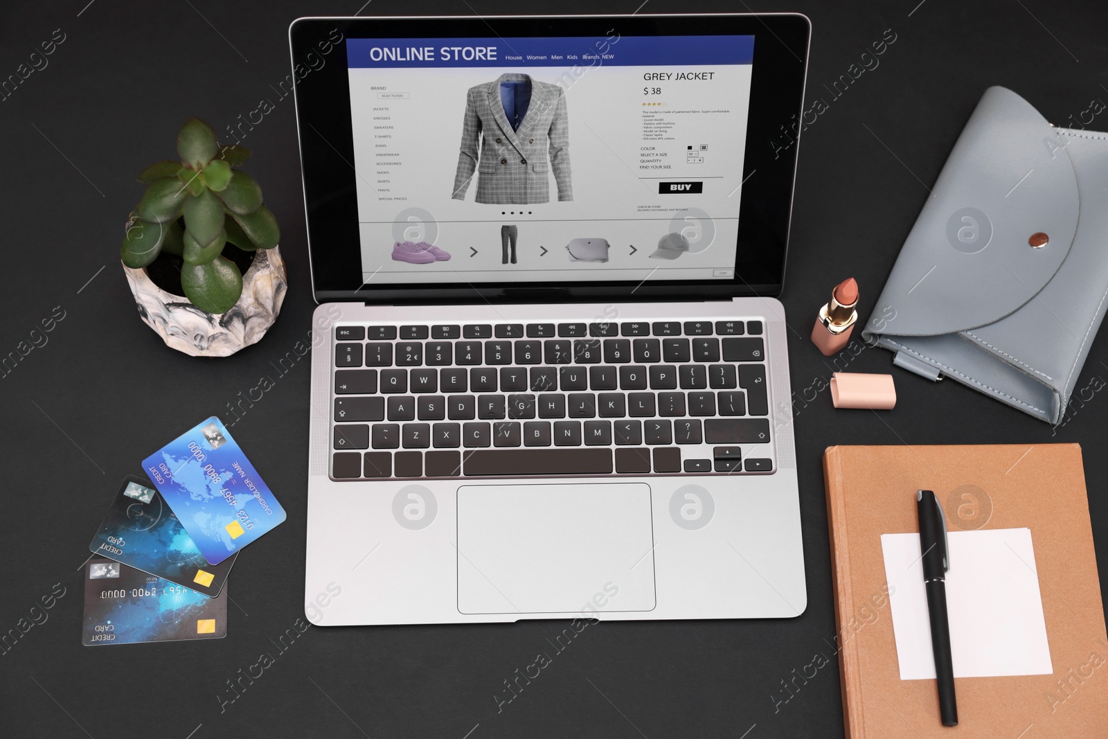 Photo of Online store website on laptop screen. Computer, credit cards, women's bag, stationery and lipstick on black background, above view