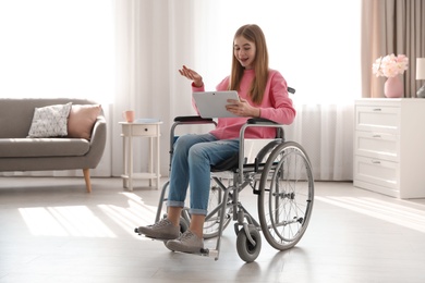 Photo of Teenage girl in wheelchair using video chat on tablet at home