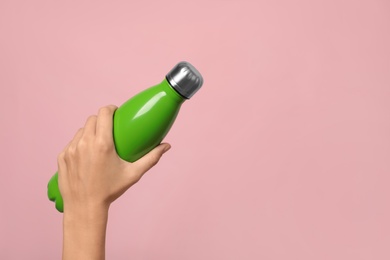 Photo of Woman holding modern green thermos on pink background, closeup. Space for text