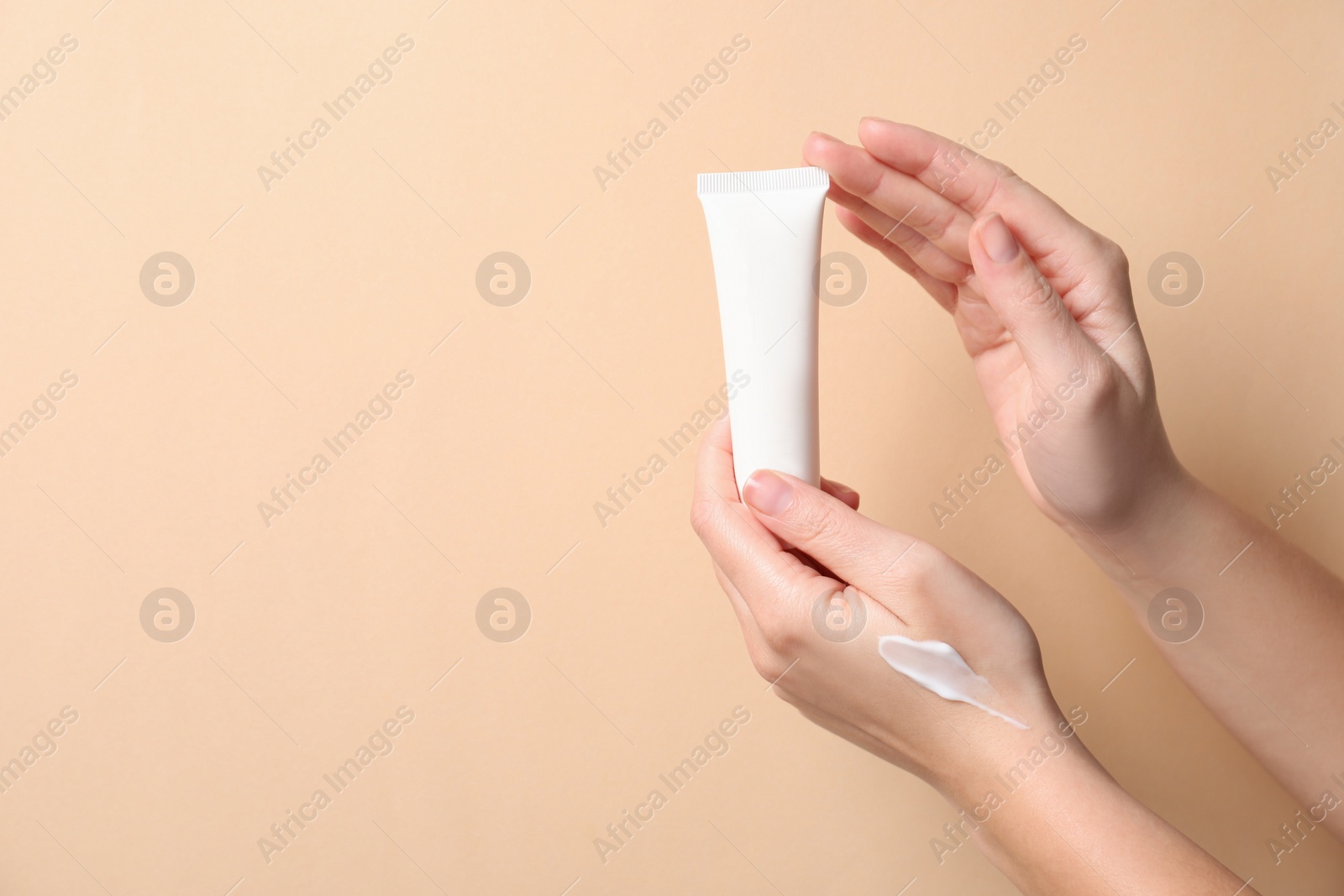 Photo of Woman with tube of hand cream on beige background, closeup. Space for text