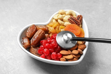 Photo of Heart shaped bowl with dried fruits, nuts and stethoscope on grey background