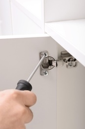 Man fixing door of white wardrobe with screwdriver, closeup