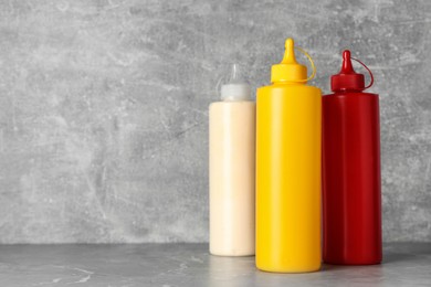 Bottles of mustard, ketchup and mayonnaise on light grey table. Space for text
