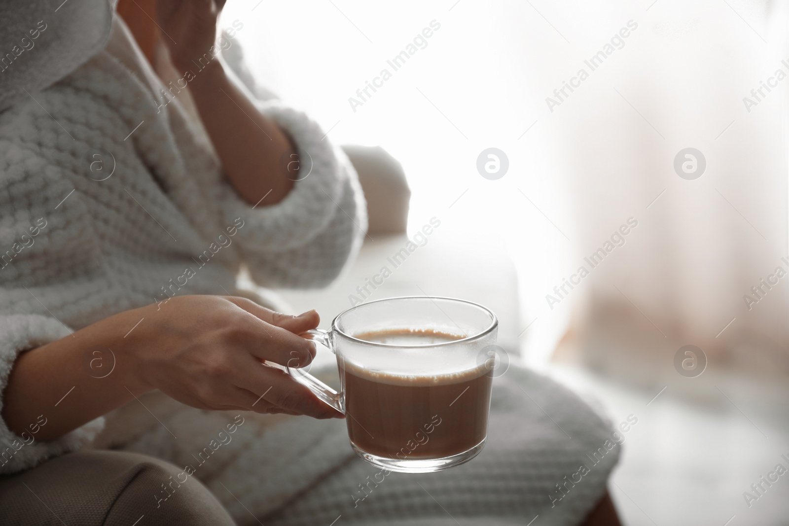 Photo of Woman with cup of hot drink on sofa at home in morning, closeup