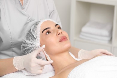 Photo of Professional cosmetologist holding skincare ampoule while working with client in clinic, closeup