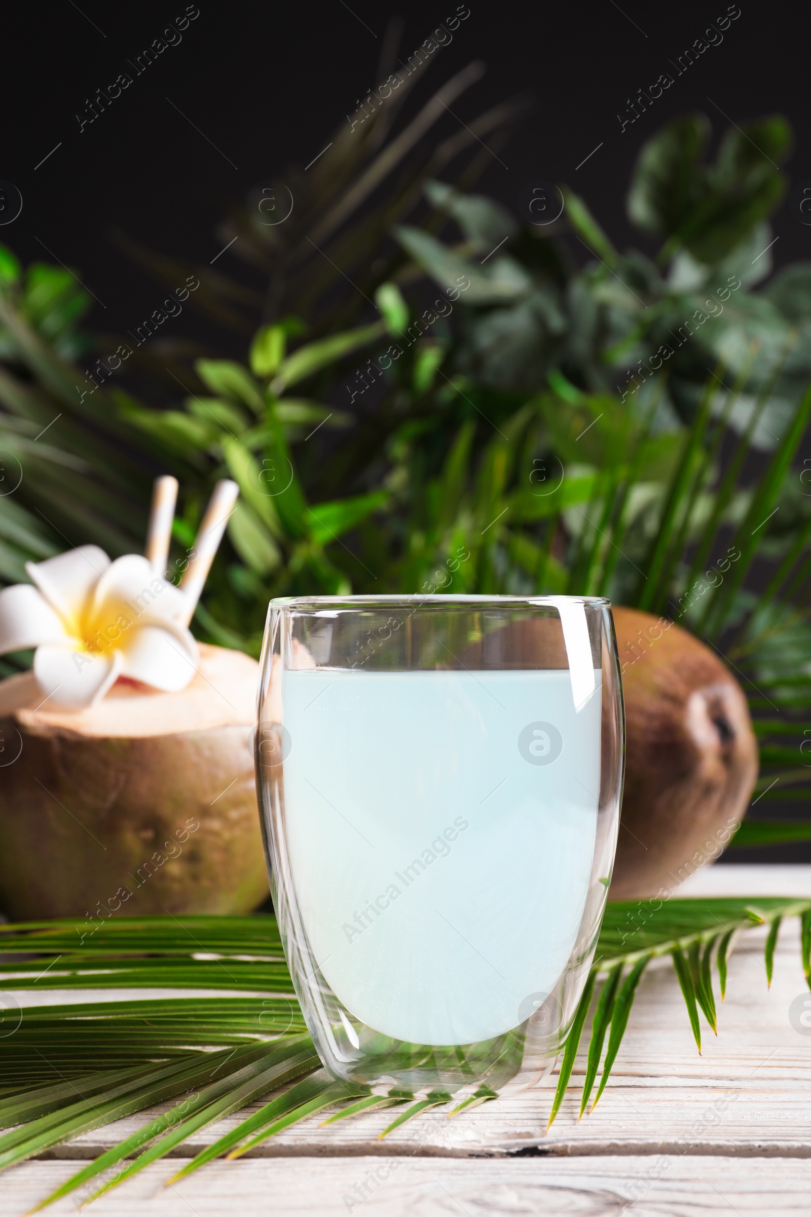 Photo of Glass of fresh coconut water and tropical palm leaf on wooden table