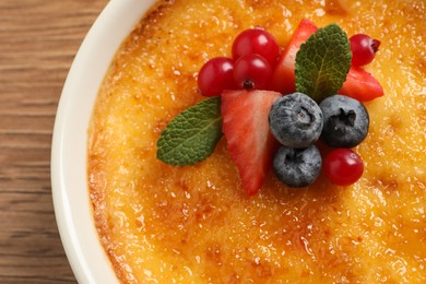 Photo of Delicious creme brulee with fresh berries on wooden table, closeup