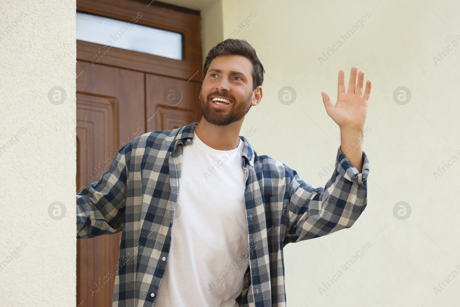 Photo of Neighbor greeting. Happy man waving near house outdoors