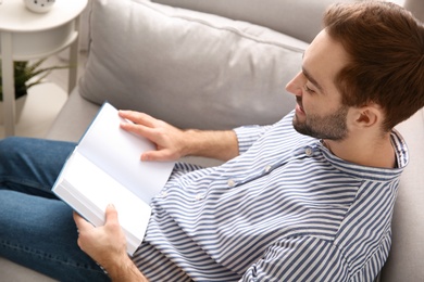 Photo of Handsome young man reading book on sofa at home