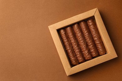 Photo of Sweet tasty chocolate bars in box on brown background, top view. Space for text