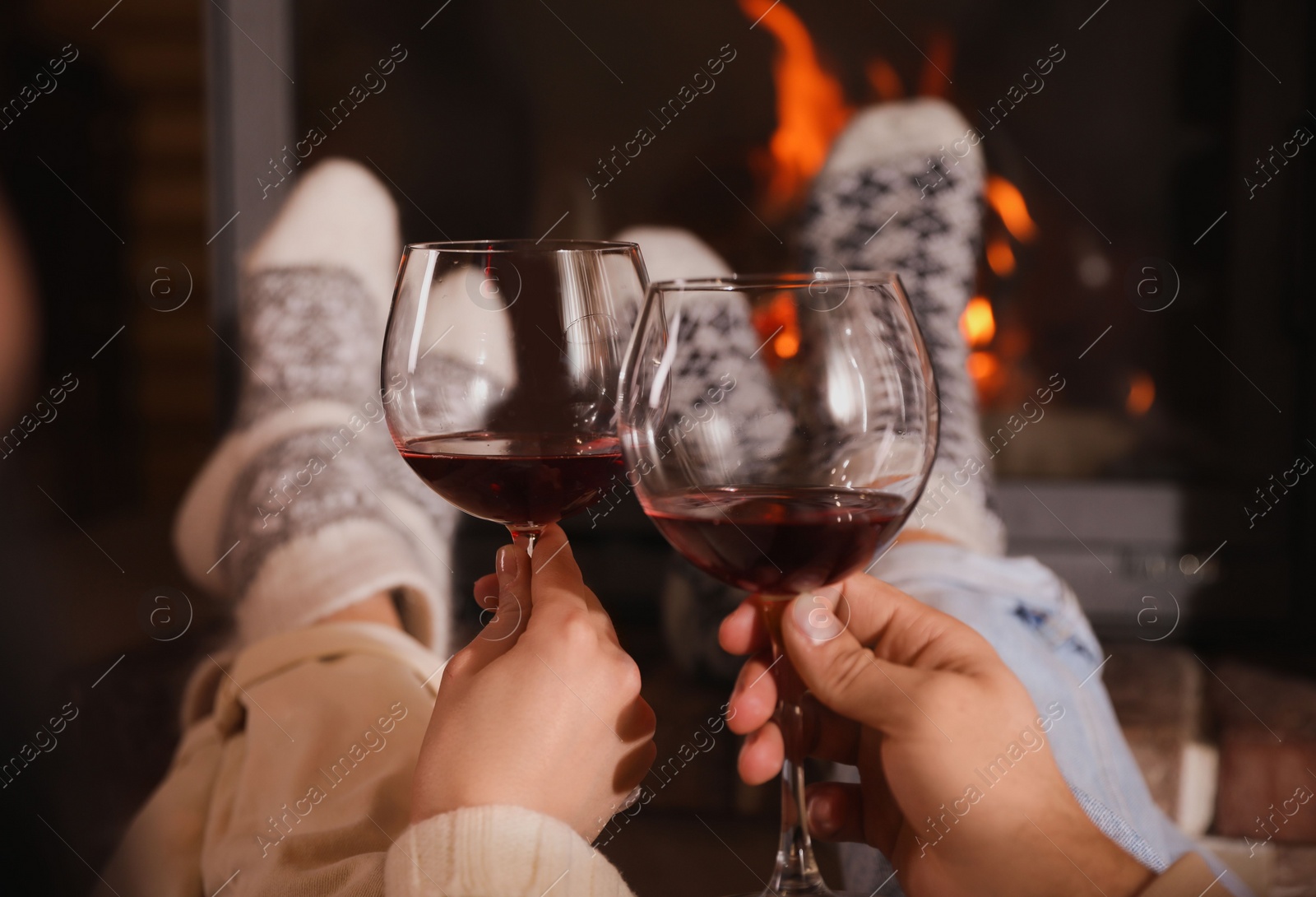 Photo of Couple with glasses of red wine near burning fireplace, closeup