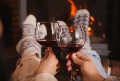 Couple with glasses of red wine near burning fireplace, closeup