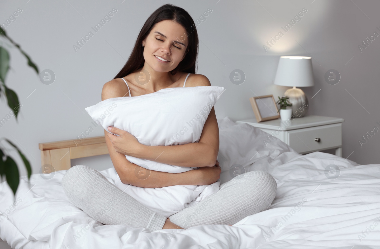 Photo of Beautiful young woman hugging pillow on bed at home