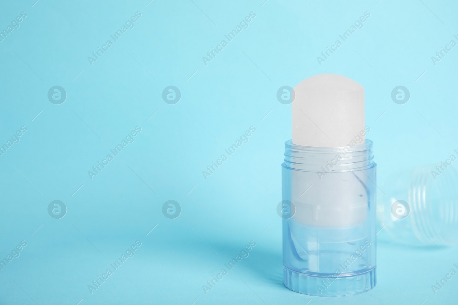 Photo of Natural crystal alum stick deodorant and cap on light blue background. Space for text