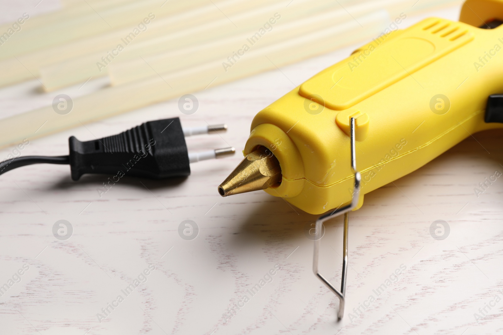 Photo of Yellow glue gun and sticks on white wooden table, closeup