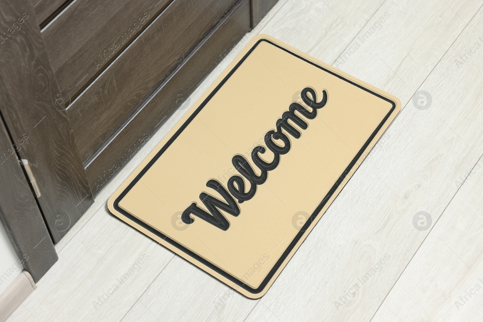 Photo of Beige doormat with word Welcome on white floor near entrance