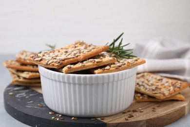 Photo of Cereal crackers with flax, sunflower, sesame seeds and rosemary in bowl on table, closeup